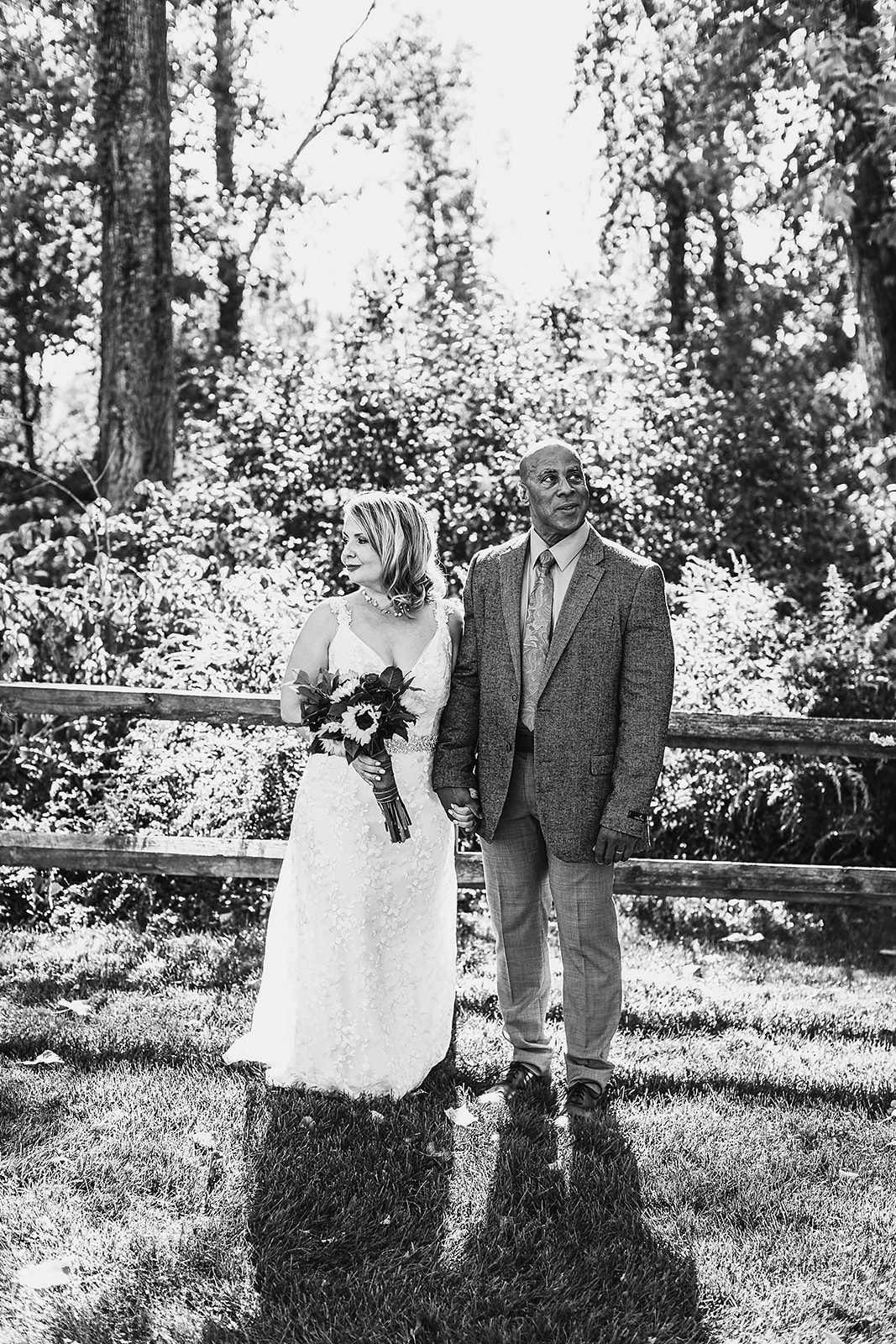 A black and white image of newlyweds holding hands along the fence at their Saratoga Winery wedding