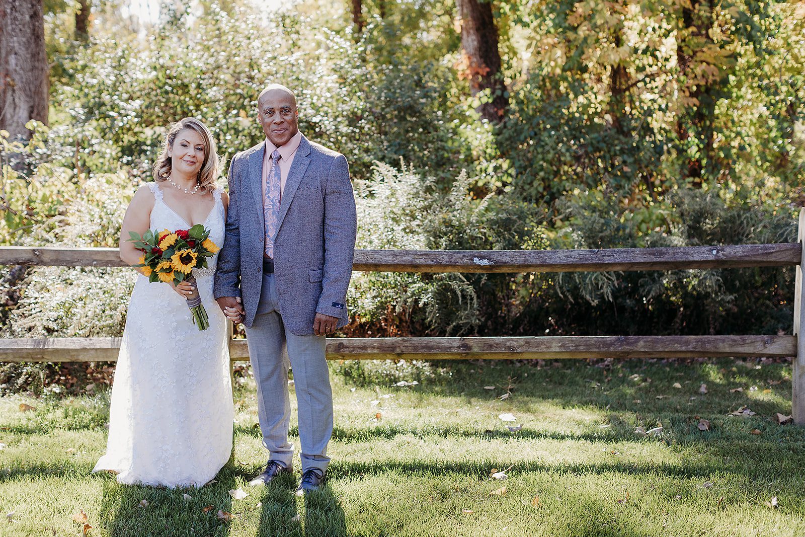 Newlyweds stand holding hands by the tree line in the lawn of the beautiful Saratoga Winery wedding venue