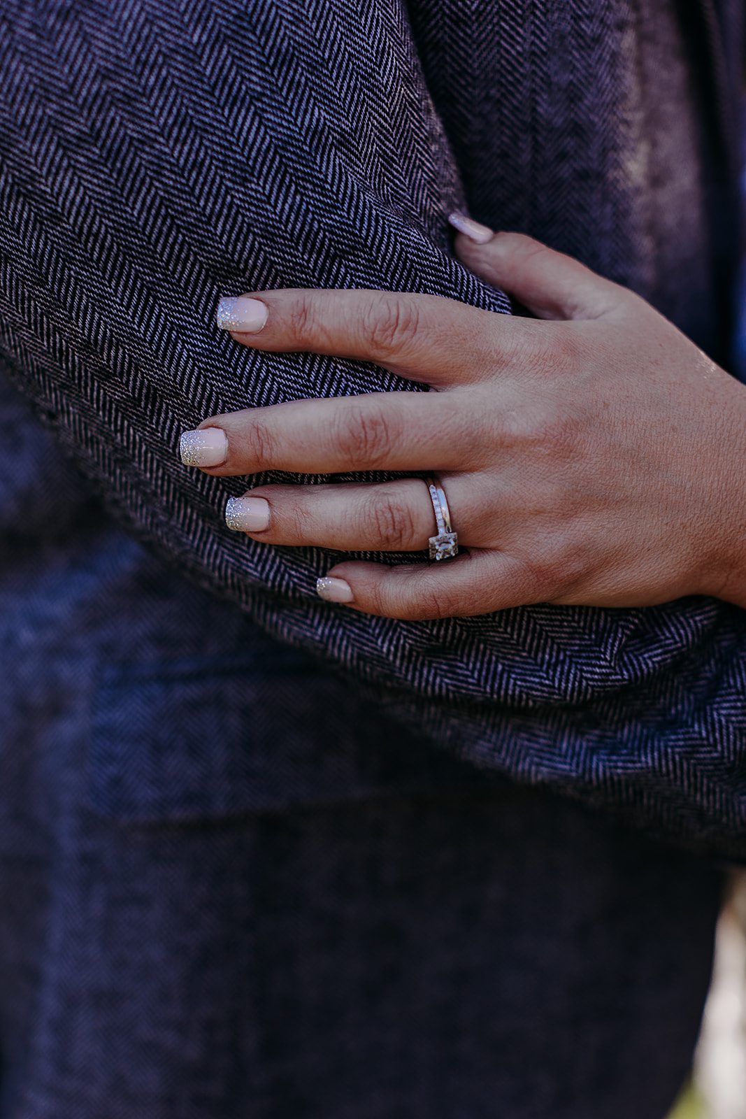 Details of a bride's hand with rings on her groom's grey suit