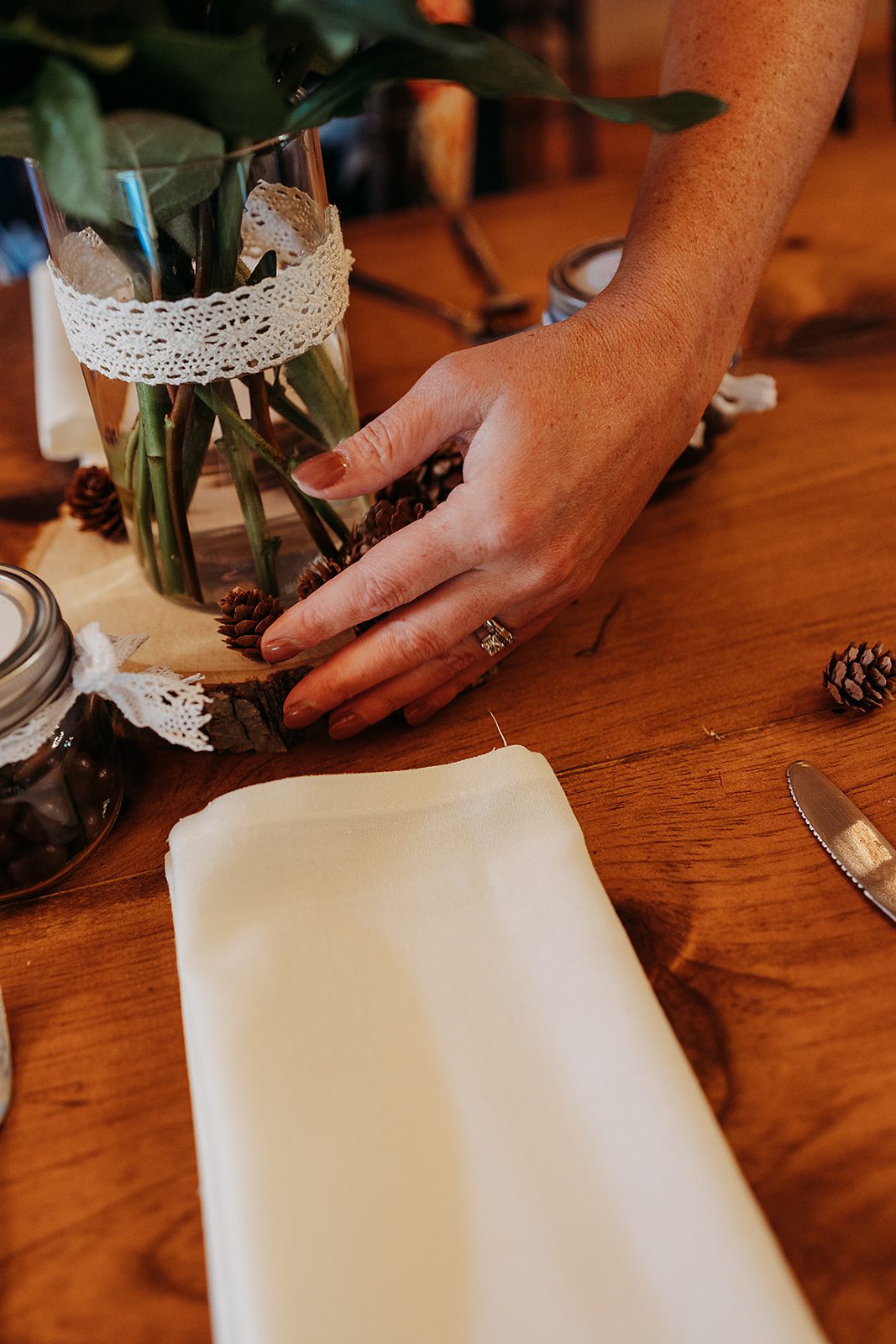 Details of a napkin on a table as a woman arranges pinecones as decorations around florals