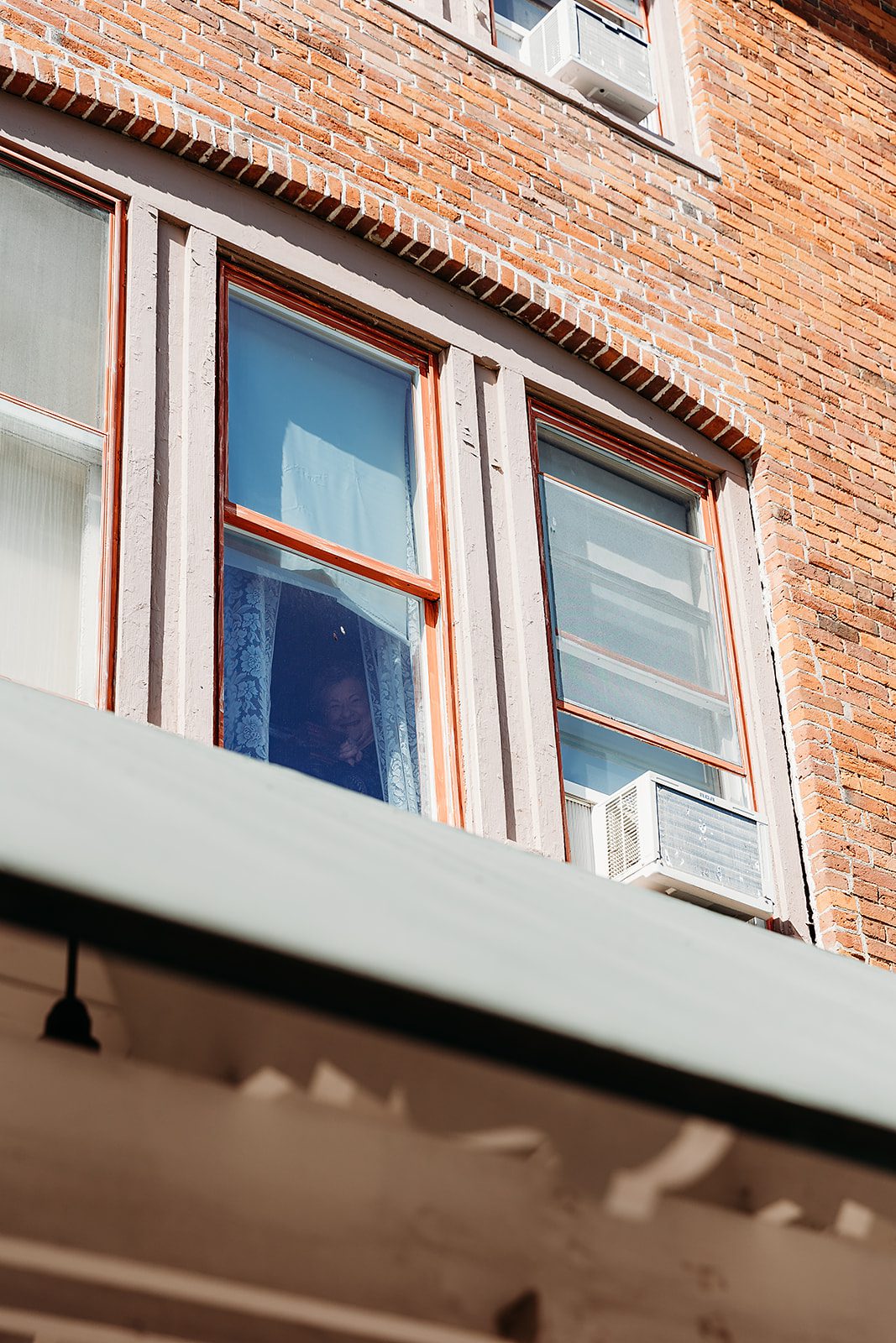 A happy grandma peeks out a window as seen from the street