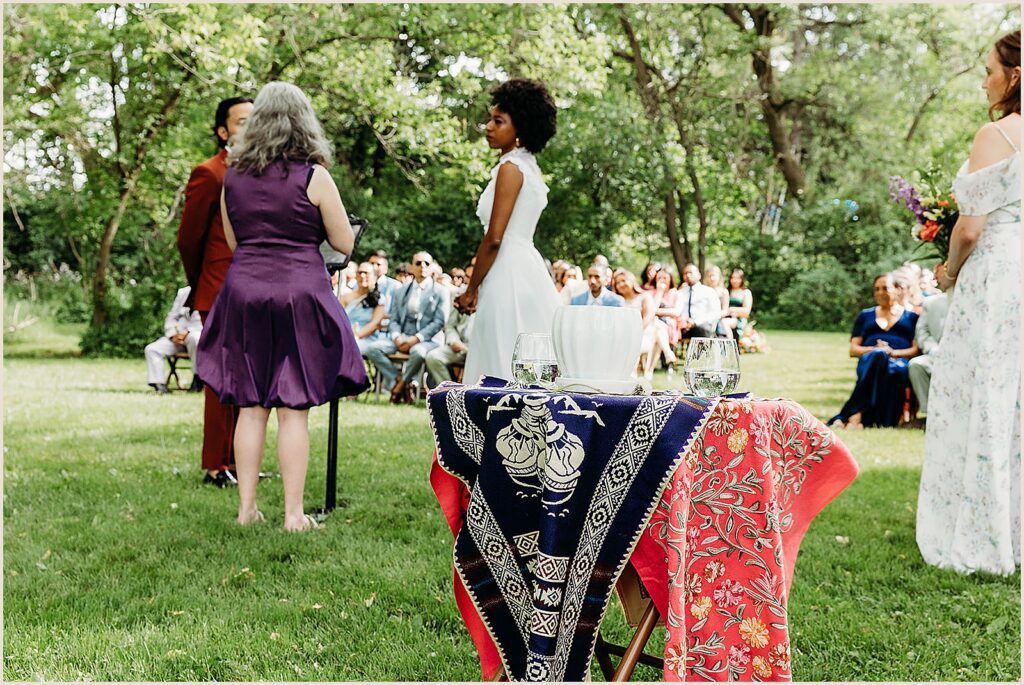 A bowl and pitcher sit on a table beside a wedding ceremony.