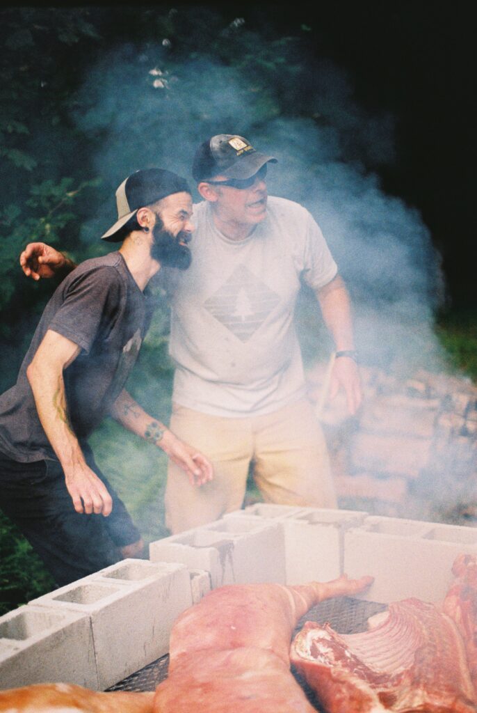 Two men stand beside a pig roasting.