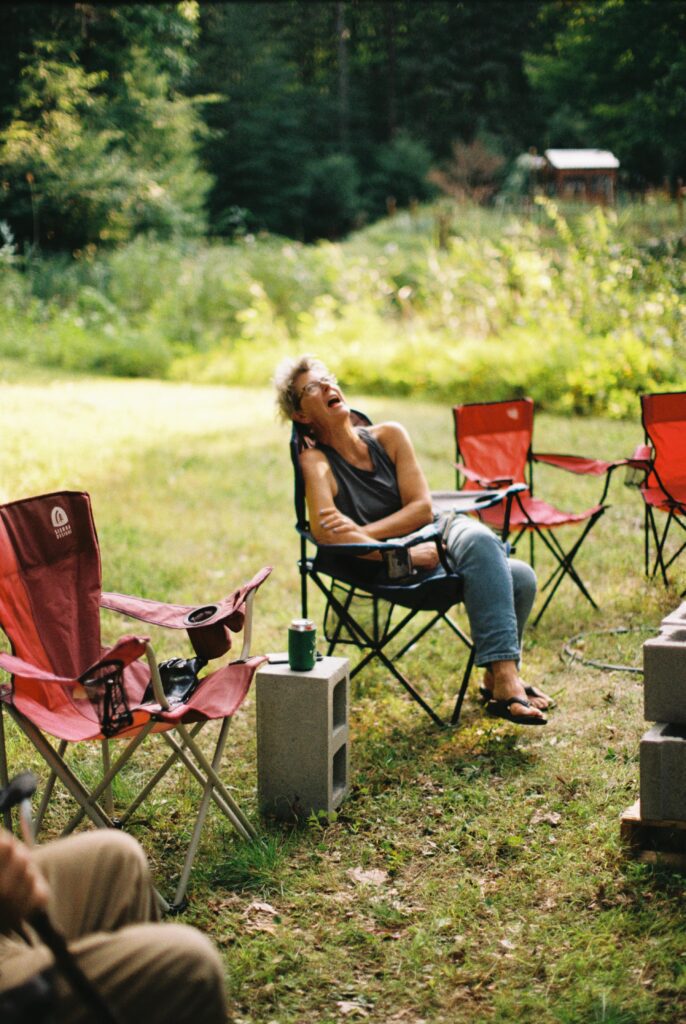 A person sits in a camping chair laughing.