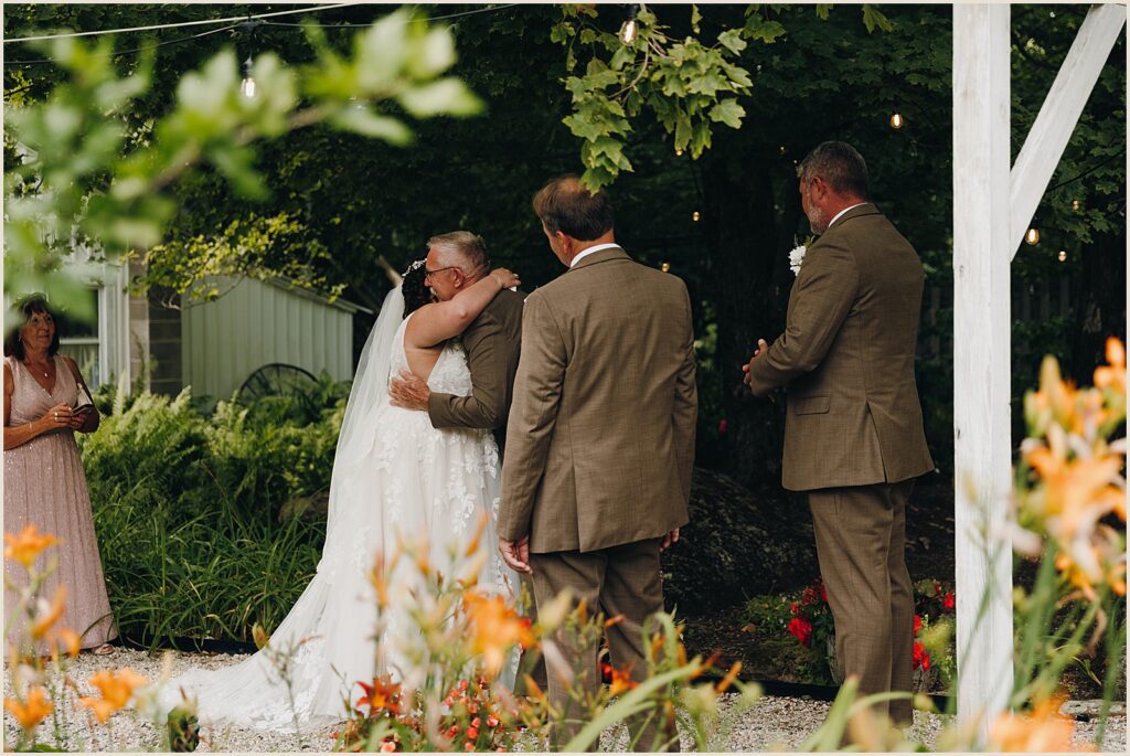A bride hugs her father in a garden.