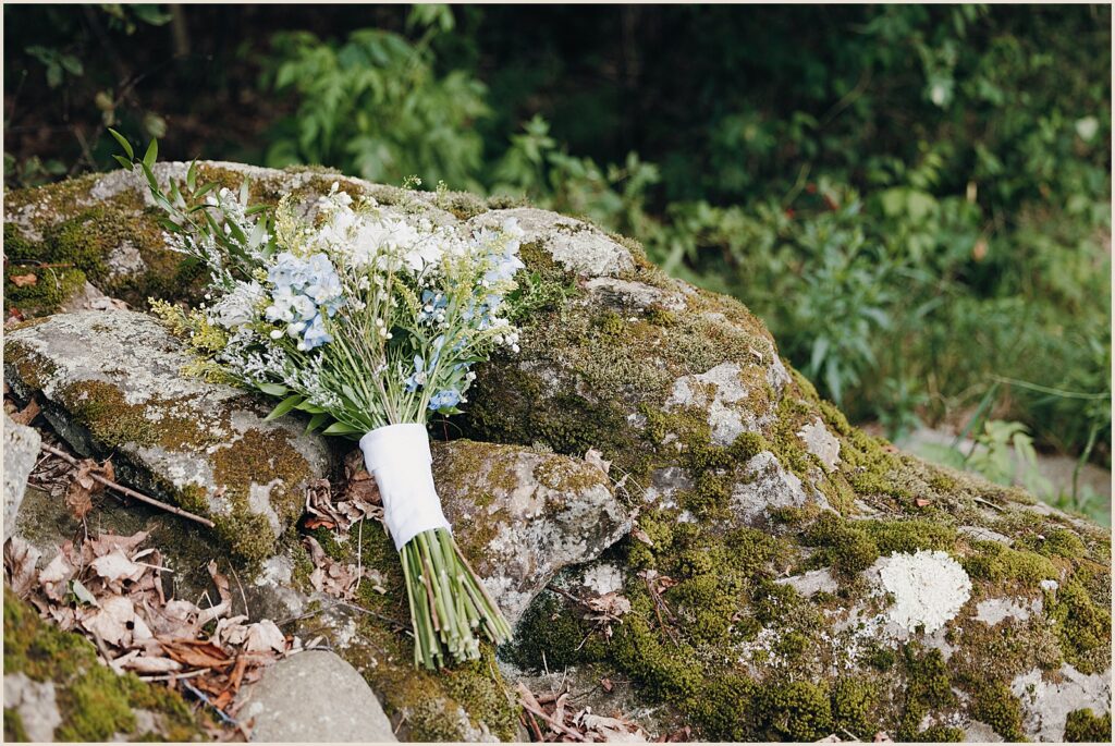 A bridal bouquet lays on a mossy boulder.