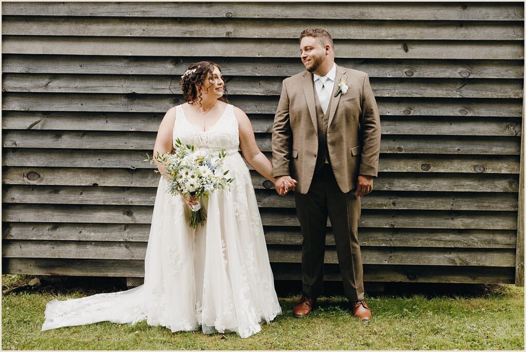 A bride and groom hold hands beside a barn.
