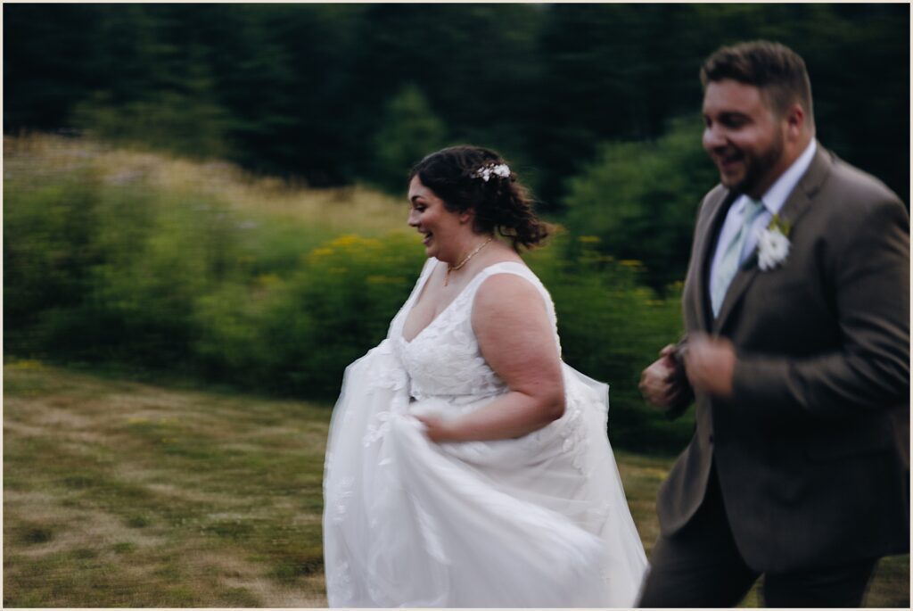 A bride and groom run through a field.