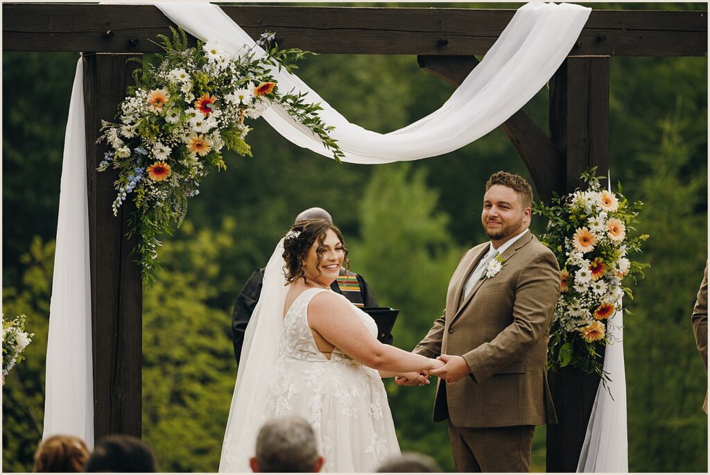 A bride and groom smile at their guests during a ceremony at Greywacke Meadows.