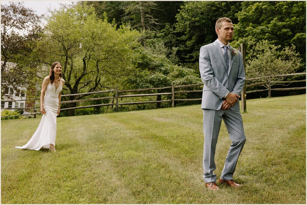 A bride approaches a groom on a lawn at a Vermont wedding venue.