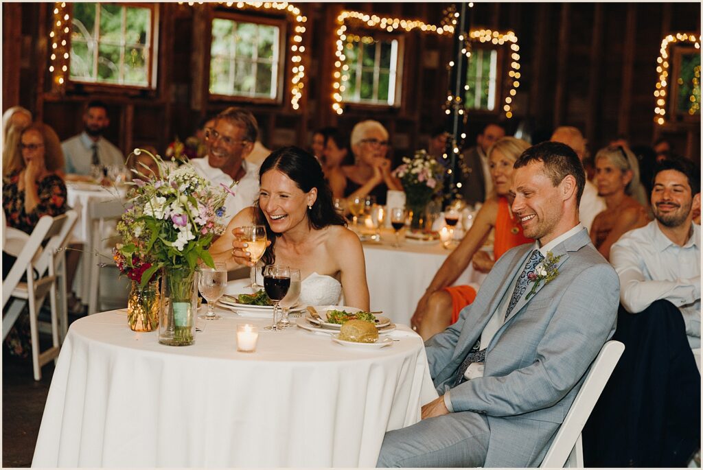 A bride and groom laugh during a speech.