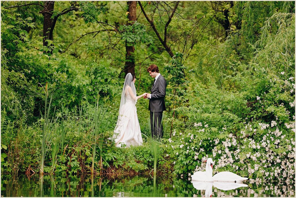 A bride and groom hold hands beside a lake at their Windrift Hall wedding.