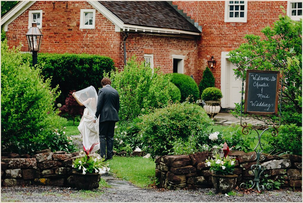 A bride and groom walk in front of a historic manor house.