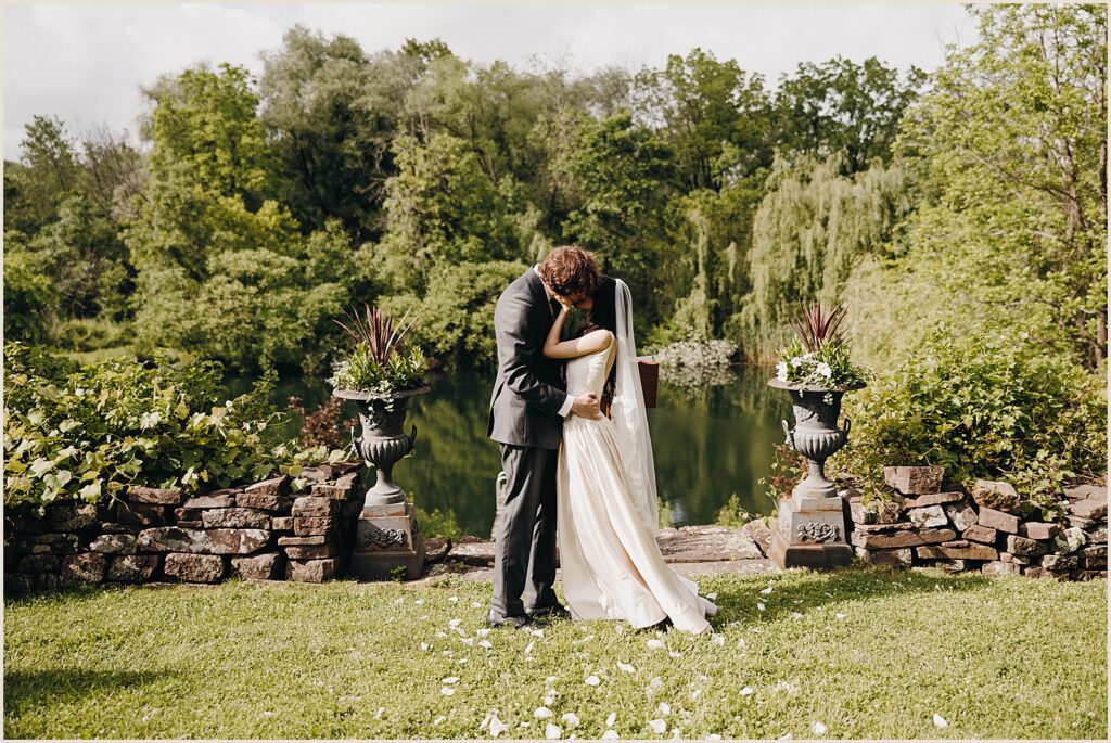 A bride and groom kiss beside a pond.