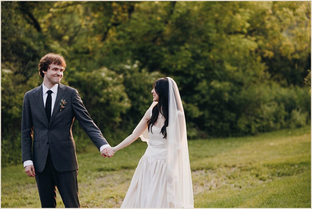 A bride and groom hold hands in a field.