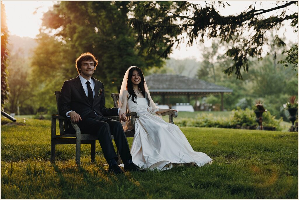 A bride and groom sit in lawn chairs holding hands.